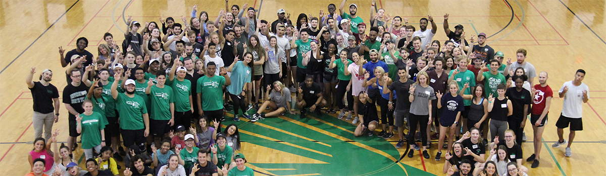 UNT Rec sports staff members and student workers are lined up on the basketball court for an overhead camera shot.